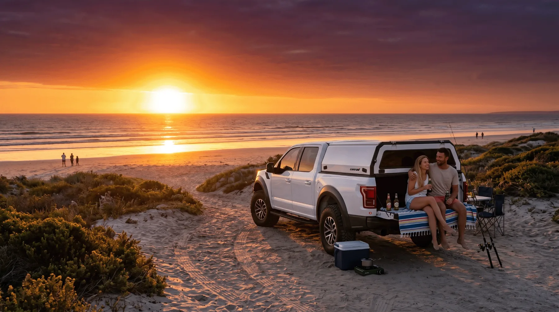 White bakkie with Canrail canopy parked at the beach at sunset with a couple relaxing on the tailgate