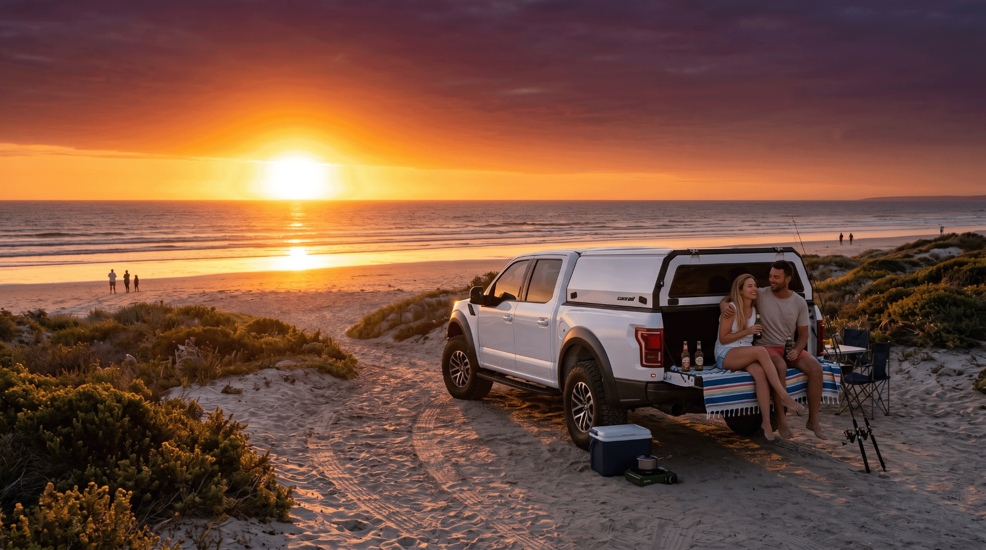White bakkie with Canrail canopy parked at the beach at sunset with a couple relaxing on the tailgate